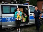 kobieta z dzieckiem na rękach stoi tyłem do policyjnego furgonu a przy niej umundurowany i uśmiechnięty policjant
