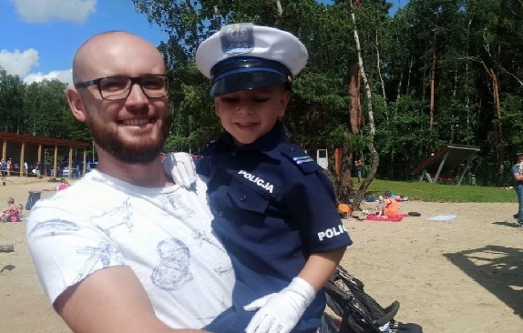 Mężczyzna trzymający na ręku dziecko przebrane w strój policjanta