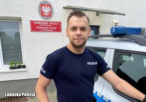 policjant stoi przed komisariatem obok radiowozu policyjnego