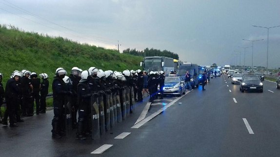 Policjanci z pododdziałów zwartych zabezpieczają zatrzymane do kontroli autokary na poboczu drogi ekspresowej.