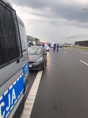 Policjanci z pododdziałów zwartych zabezpieczają zatrzymane do kontroli autokary na poboczu drogi ekspresowej.