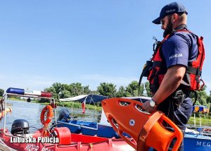 policjant stoi przy łódce z bojką w ręku obok jeziora