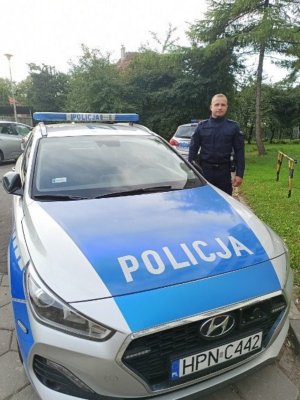 Umundurowany policjant stoi z boku radiowozu