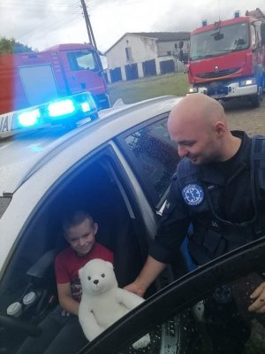 Asp. Dawid Banaszak wręcza siedzącemu w radiowozie chłopcu maskotkę