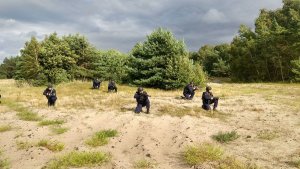 ćwiczenia: rozstawieni w terenie policjanci klęczą na jednym kolanie, w rekach trzymają broń