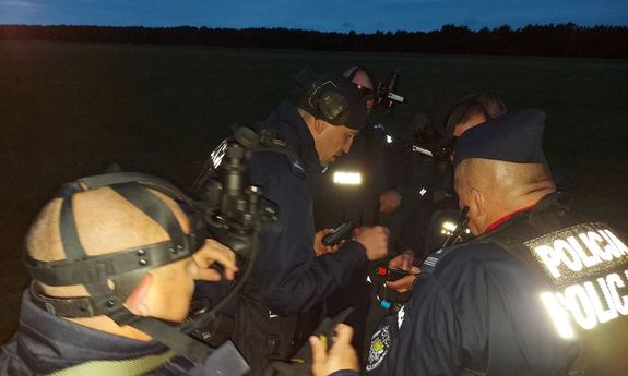 ćwiczenia, widok nocny: pięciu umundurowanych policjantów stoi w terenie w grupce i sprawdzają trzymany w rękach sprzęt.