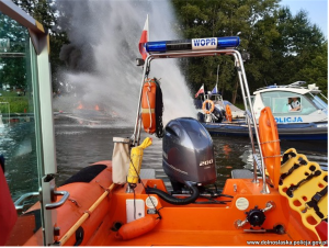 policyjna łódź tworzy strumień wody gaszący płonącą łódź