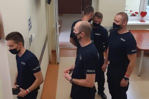 Policjanci stoją w kolejce do punktu rejestracji, zwróceni twarzami w lewą stronę.