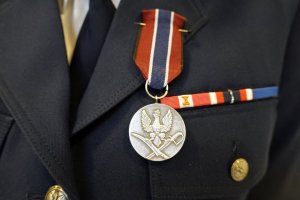 Medal „Pro Patria”, awers, przedstawiający wizerunek stylizowanego orła Rzeczypospolitej z przełomu XVII i XVIII wieku, który jest oparty jest po lewej stronie o kosę bojową, a po prawej o szablę polską, wzór 1921/22.