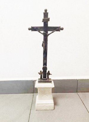 Metalowy krzyż na kamiennym postumencie w kolorze białym.