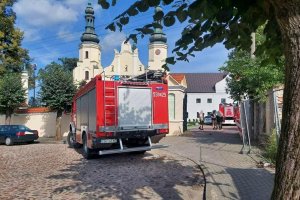 Przed bramą klasztoru stoi wóz bojowy straży pożarnej, samochody osobowe.