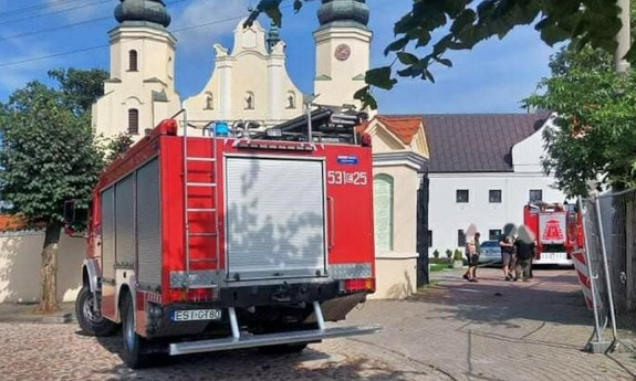 Przed bramą klasztoru stoi wóz bojowy straży pożarnej, samochody osobowe.