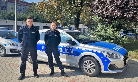 Policjant i policjantka stoją koło radiowozu.