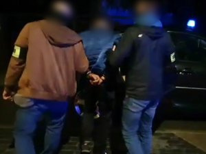 Dwaj policjanci po cywilnemu prowadzą skutego zatrzymanego mężczyznę.