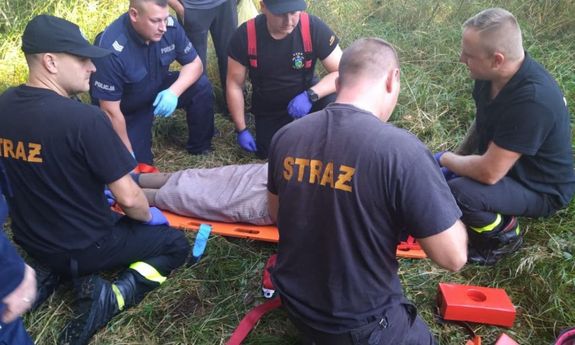 strażacy i policjant pochylają się nad leżącą kobietą