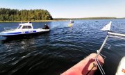 Policyjna łódź służbowa na jeziorze, w tle łódź WOPR i przewrócona żaglówka, na której jest dwóch mężczyzn