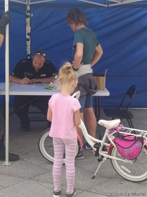 Policjant notuje w rejestrze dane, widać dziewczynkę i kobietę, które przyszły oznakować rower.