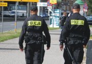 policyjny patrol - dwaj policjanci w czarnym moro z żółtym napisem na plecach &quot;Policja&quot; idą ulicą - widok z tyłu