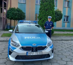 umundurowany policjant stojący przy oznakowanym radiowozie zaparkowanym na parkingu przed wieluńską komendą