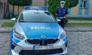 umundurowany policjant stojący przy oznakowanym radiowozie zaparkowanym na parkingu przed wieluńską komendą
