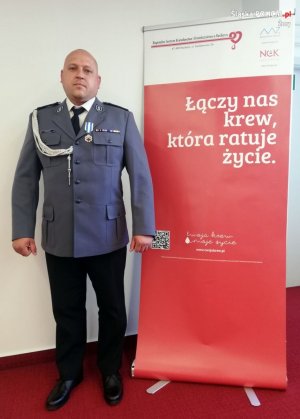 Policjant stoi przy roll-upie Regionalnego Centrum Krwiodawstwa i Krwiolecznictwa w Raciborzu.