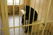 mężczyzna siedzący na pryczy w celi, za kratami
