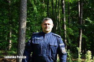 Policjant podczas poszukiwań, rozglądający i poruszający się po lesie wśród drzew