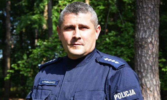 Policjant na pierwszym planie podczas poszukiwań w lesie, z tyłu widoczne drzewa