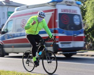 Jadący policjant rowerzysta na tle karetki pogotowia.