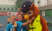 dzieci w niebieskich strojach sportowych tulą się do maskotki policyjnej