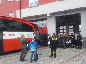 policjanci, żołnierze i strażacy stoją przed krwiobusem czekając na oddanie krwi