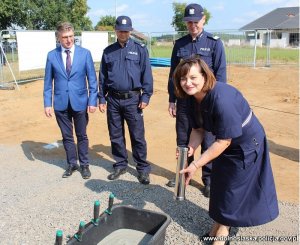 wmurowanie kamienia węgielnego pod budowę komisariatu modułowego w Prochowicach. Kobieta w sukience trzyma w dłoni tubę, za nią stoją trzej mężczyźni: jeden w garniturze i dwóch w mundurach