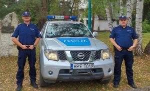 dwaj policjanci stoją przy radiowozie