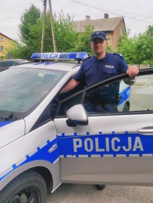 zdjęcie przedstawia policjanta stojącego przy radiowozie