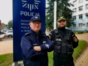 policjant i strażnik miejski, w tle budynek komendy policji