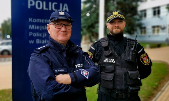 policjant i strażnik miejski, w tle budynek komendy policji