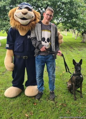 Chłopiec trzyma na smyczy psa i wraz z komisarze lwem pozuje do zdjęcia