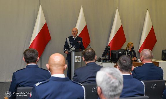 Za mównicą Komendant Główny Policji obok siedzi Komendant Rektor WSPol. Na sali siedzą uczestnicy uroczystości - widok z tyłu