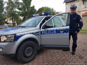 Umundurowany policjant stoi przy oznakowanym radiowozie.