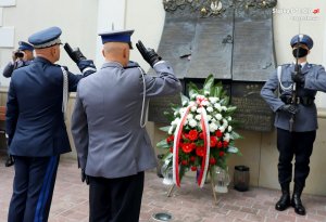 Salutujący policjanci oraz złożony wieniec przy płaskorzeźbie