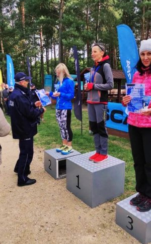 Zdjęcie przedstawia podium wraz zawodnikami oraz policjanta wręczającego medal.&quot;&gt;