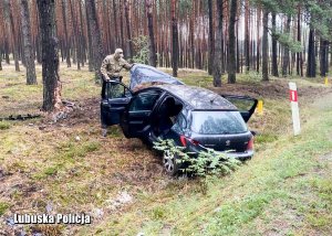 Zniszczone auto leżące w rowie przy leśnej drodze a obok niego kontrterrorysta