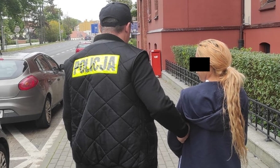 policjant trzyma zatrzymaną skutą kajdankami