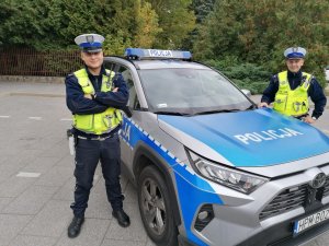 Umundurowani policjanci stojący przy radiowozie.