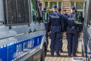 stojący za statywem z mikrofonem umundurowany generał - Zastępca Komendanta Głównego Policji nadinsp. Roman Kuster i widoczne plecy czterech umundurowanych policjantów i policyjne radiowozy