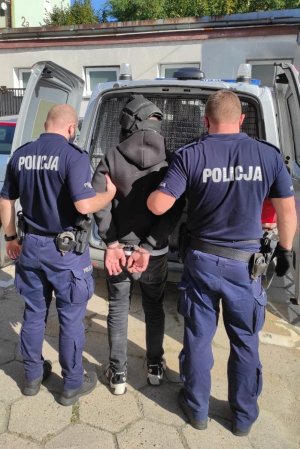 Policjanci prowadzą zatrzymanego do radiowozu.