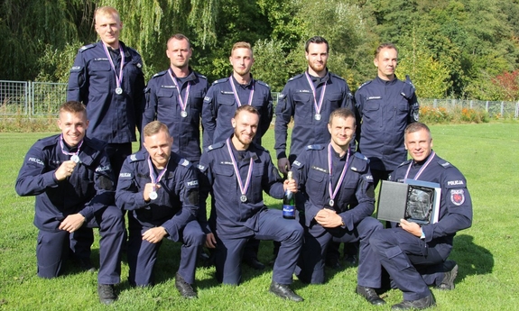 Zdjęcie zbiorowe dziesięciu policjantów w mundurach. Ma szyjach mają założone medale na wstążkach. Jeden trzyma w ręku statuetkę umieszczoną w skrzyneczce