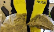 policjant w żółtej kamizelce z napisem Policja trzyma w rękach dwa worki foliowe z narkotykami