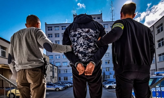 dwaj policjanci z zatrzymanym mężczyzną zakutym w kajdanki