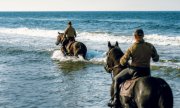 Jeźdźcy na koniach jadą brodząc w morzu.